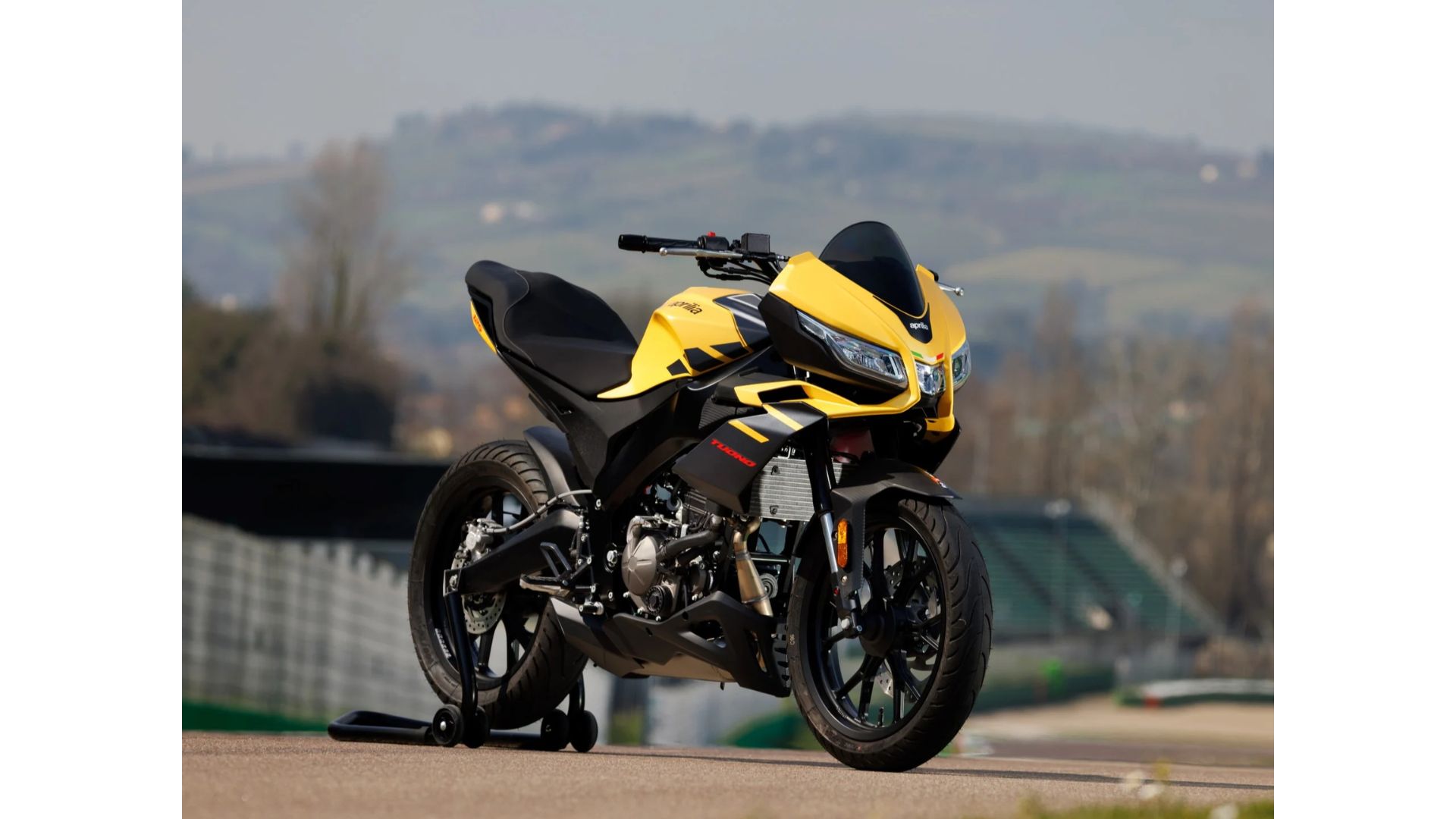 Aprilia Tuono 125 v rumeni barvi na dirkališču – športni motocikel z aerodinamičnim oklepom in sodobnim videzom