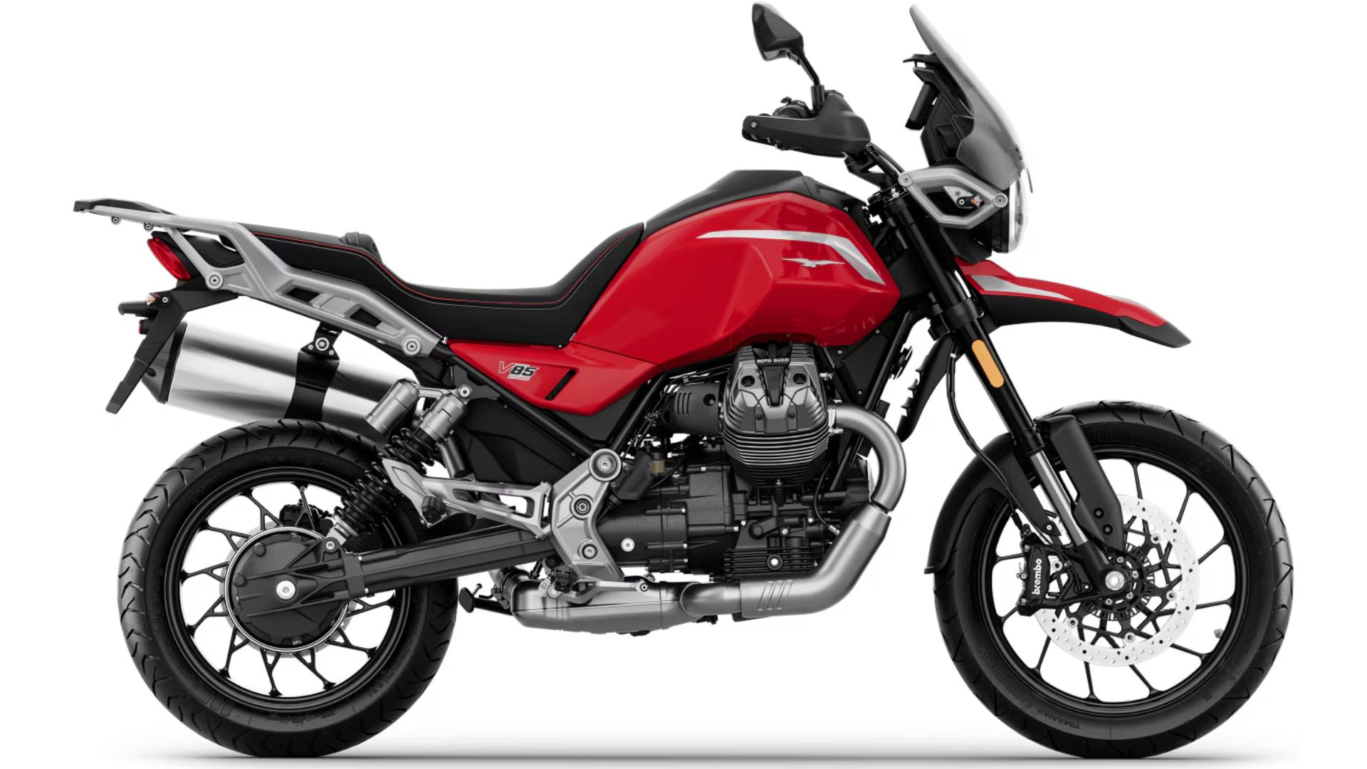 Stranski profil motocikla Moto Guzzi V85 TT v sivi barvi z rdečim logotipom, dvema izpušnima cevema, prednjim in zadnjim diskovnim zavoram ter litimi platišči, na belem ozadju.