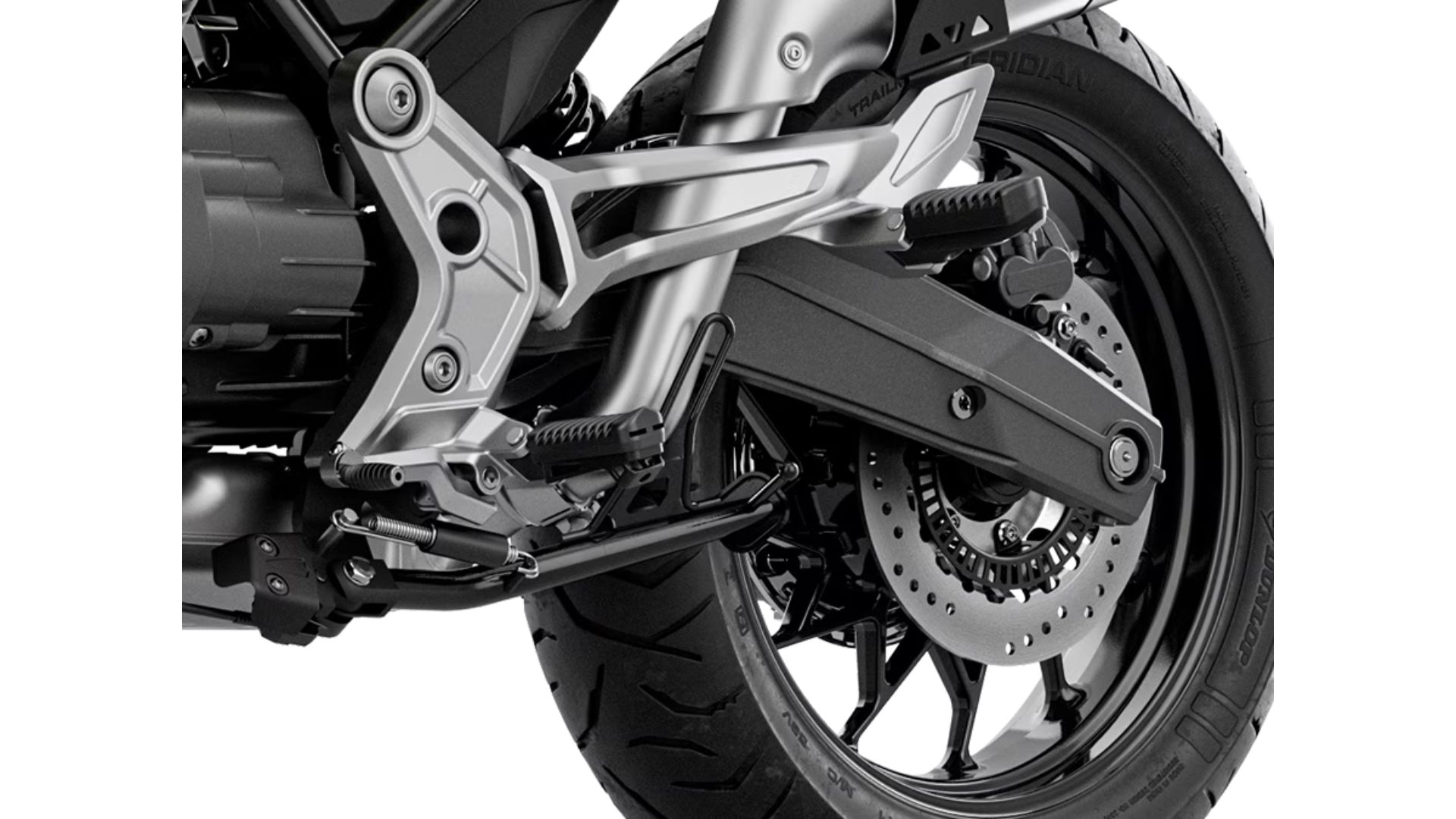 Detajl zadnjega dela motocikla Moto Guzzi V85 TT z aluminijastim izpušnim sistemom, zadnjo lučjo in diskovnimi zavorami, s terenom v ozadju.