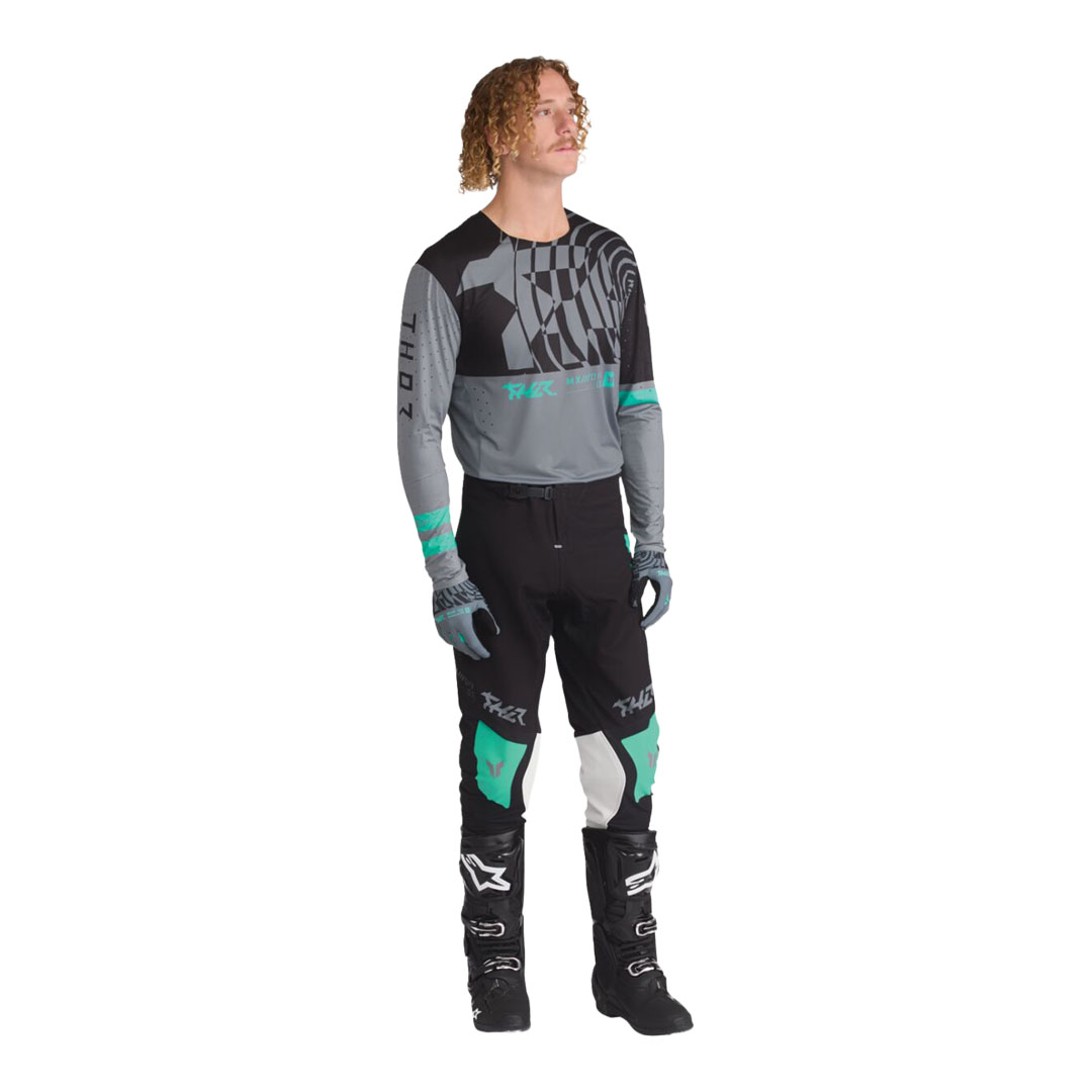 Model nosi motokros hlače Thor Sportmode Mind Control, prikazane spredaj pod kotom, z mint poudarki na kolenih in črnim krojem.